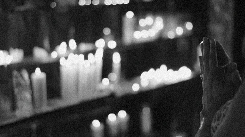 Imagem de uma pessoa com as mãos em posição de oração em frente à diversas velas, representando a religiosidade