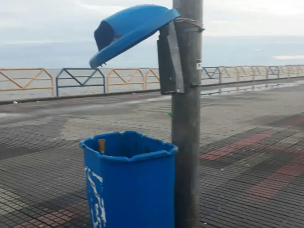Imagem de uma lixeira pública danificada por uma pessoa, configurando o crime de dano qualificado.
