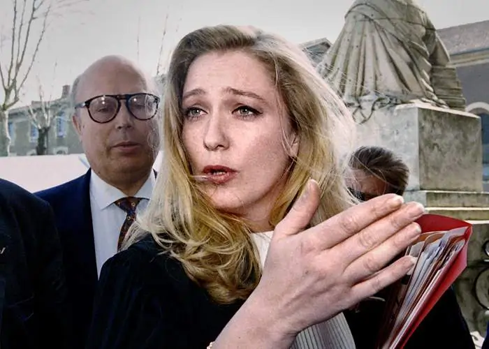 Imagem de Marine Le Pen, uma mulher branca, loira, de cabelos longos e olhos verdes. Ela está segurando uma pasta vermelha com documentos.