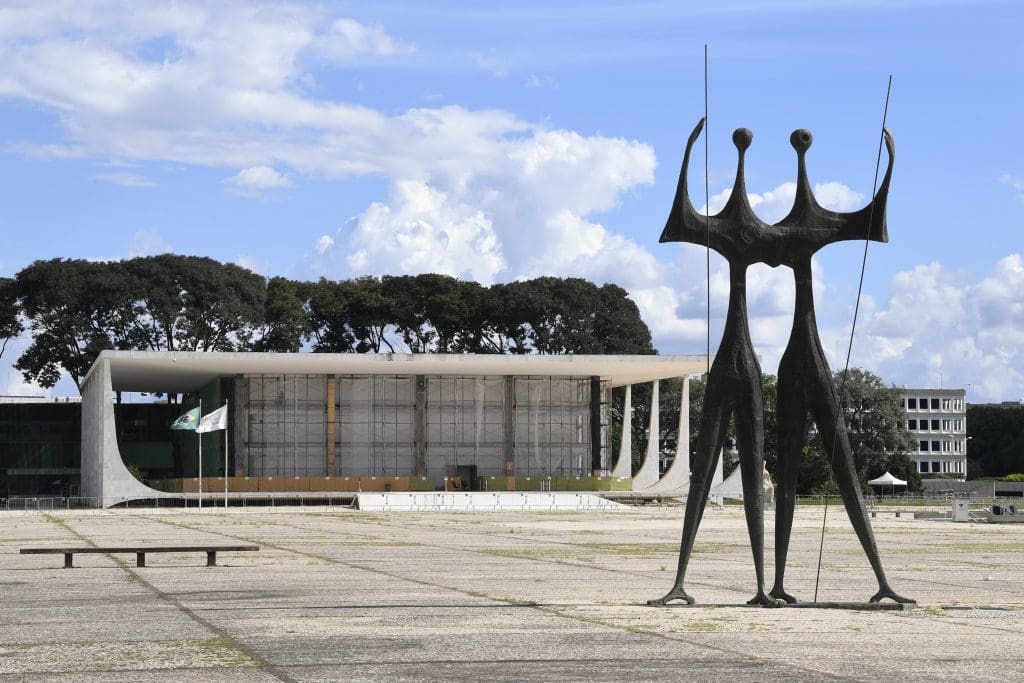 Alt text: Foto da Praça dos Três Poderes, em Brasília, com o monumento “Os Candangos” em primeiro plano.