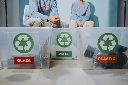 Imagem de três caixas de separação de vidro, papel e plástico. Texto: Economia circular: repensando produção e consumo no século XXI