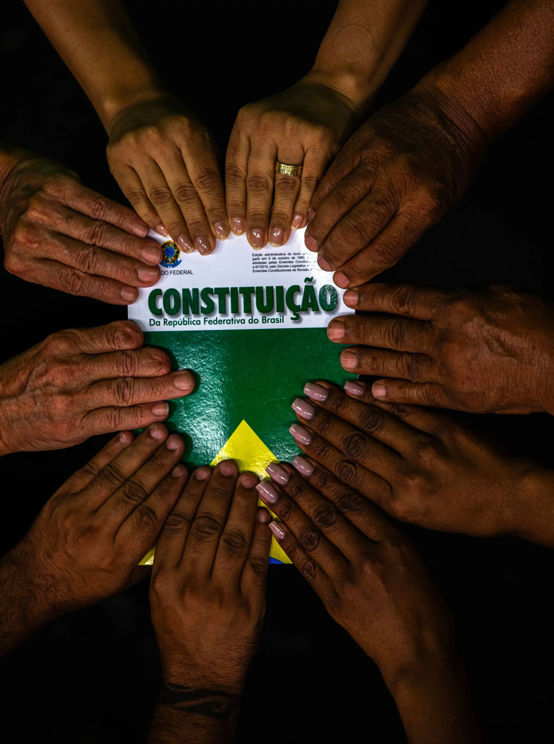 Imagem de vãrias mãos diferentes segurando a Constituição brasileira. 