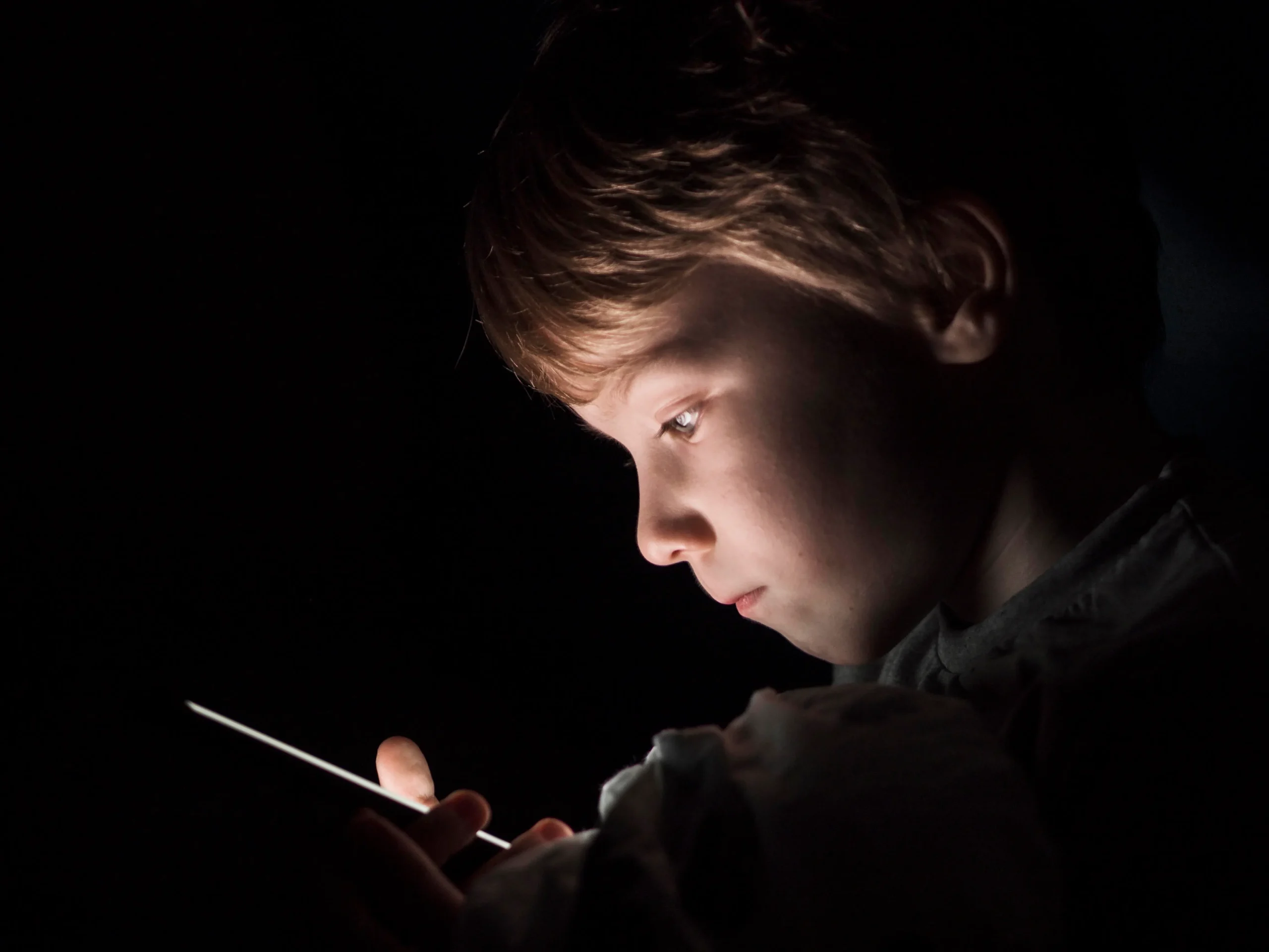 Criança usando celular com luz da tela no rosto.