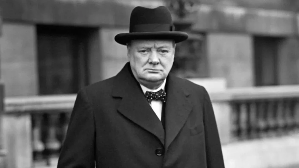 Foto em preto e branco de Winston Churchill - um homem de meia idade usando terno, gravata borboleta e chapéu